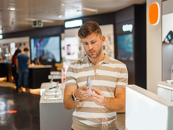 Toepassing van phigital in retail omgeving. Afbeelding toont jonge man met gsm te midden van andere high tech